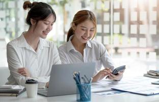 duas trabalhadoras jovens empresárias trabalhando juntas em seus laptops leem telas com rostos sorridentes em ângulos altos. foto