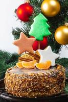 close-up de bolo de natal com pão de gengibre e tangerinas no fundo da árvore de natal foto