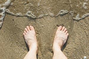 pés masculinos caucasianos asiáticos na areia com uma onda entra, no feriado. foto