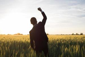 conceito de vencedor, feliz jovem empresário saltar com as mãos levantadas nos campos, plantas de trigo de verão foto