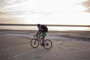 turista de bicicleta com mochilas e capacete viaja no deserto em sua bicicleta ciclocross durante o pôr do sol foto