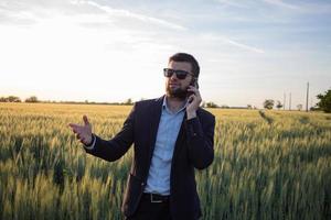 empresário em campos de trigo de verão usando tablet durante o pôr do sol, homem de terno com computador compacto foto