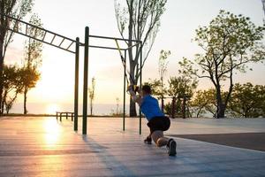 treino com tiras de suspensão no ginásio ao ar livre, treinamento de homem forte no início da manhã no parque, nascer ou pôr do sol no fundo do mar foto