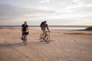 dois jovens do sexo masculino em uma bicicleta de turismo com mochilas e capacetes no deserto em uma viagem de bicicleta foto