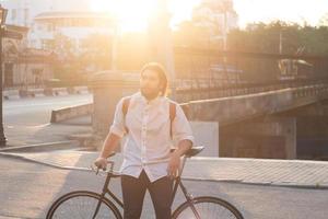 jovem barbudo com mochila de couro andando com bicicleta preta foto