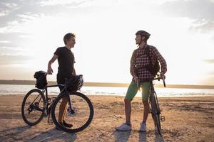 dois jovens do sexo masculino em uma bicicleta de turismo com mochilas e capacetes no deserto em uma viagem de bicicleta foto