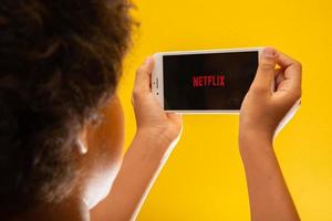 ribeirão preto, são paulo brasil por volta de novembro de 2019 abrindo o ícone do aplicativo netflix no iphone 8 plus menino descansando com o celular nas mãos e o logotipo da netflix na tela. foto