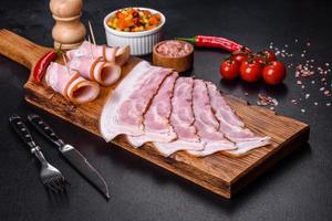 fatias de delicioso bacon cru ou salgado com especiarias, sal, legumes e ervas em uma tábua de madeira foto