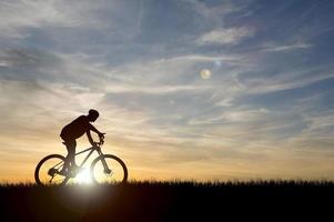 silhueta de um ciclista em um belo prado à noite. ideias de férias de bicicleta foto