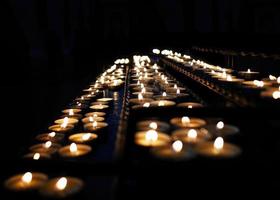 fileiras de pequenas luzes de velas na igreja de religião de fundo escuro foto