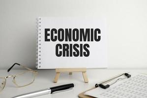 palavras de crise econômica no bloco de notas no cavalete e óculos. foto