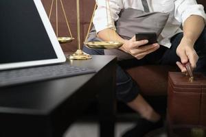 contexto de justiça e lei. mão de advogado masculino sentado no sofá e trabalhando com telefone inteligente, teclado de encaixe de computador tablet digital com martelo e documento na mesa de estar em casa