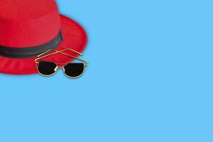 chapéu vermelho, óculos de sol preto-marrom em um fundo azul. conceito de viagem de verão foto