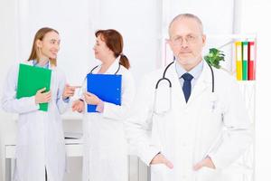 médico posando no escritório, ele está usando um estetoscópio, equipe médica em segundo plano. conceito de medicina de qualidade. espaço de cópia foto