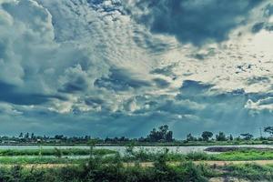 bela luz em nuvens de tempestade escuras e dramáticas após a chuva. campo de plantas verdes e lagoa sobre céu azul dramático. paisagem de céu de natureza e nuvens, fundo impressionante dramático, conceito de relaxamento foto