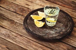 copo de tequila com rodelas de limão em um fundo de madeira foto