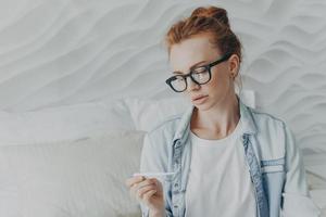 futura mãe com cabelo ruivo natural olha atentamente para o resultado positivo do teste de gravidez foto