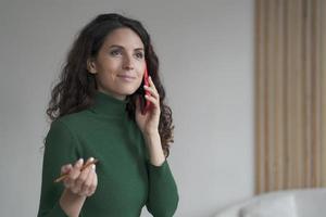 atraente jovem empresária espanhola desfrutando de conversa telefônica, usando smartphone no trabalho foto