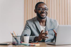 alegre empresário afro-americano usando óculos e blazer elegante fazendo videochamada no laptop