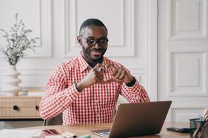 empresário romântico afro-americano olhando para laptop com videochamada mostrando o símbolo do coração com as mãos foto