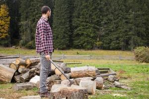 jovem macho na floresta cortando madeira com machado de aço, paisagem do país com lenhador foto