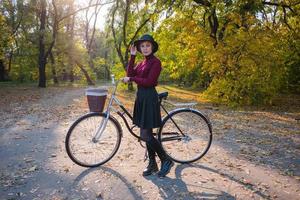 jovem no parque de outono leu livro, linda mulher ruiva com bicicleta na grama verde foto