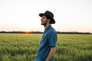 jovem agricultor masculino sozinho no campo de trigo durante o pôr do sol foto