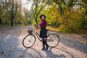 jovem no parque de outono leu livro, linda mulher ruiva com bicicleta na grama verde foto