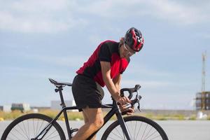 ciclista em treinamento de capacete e roupas esportivas sozinho na estrada rural vazia, campos e árvores foto