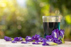 copo de vidro de água de flor de ervilha borboleta com borrão de bokeh verde claro. foto