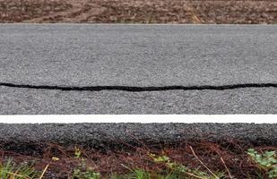 a superfície da estrada asfaltada racha perto da linha branca. foto