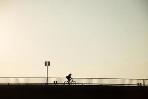 bicicleta silhueta do ciclista na ponte contra o pôr do sol, paisagem urbana minimalista foto