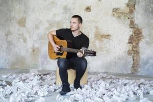 jovem macho com guitarra no quarto vazio, músico e compositor sozinho no estúdio foto