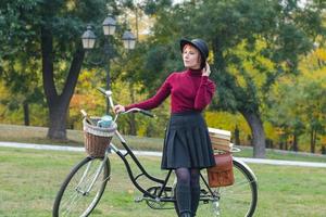 jovem no parque de outono leu livro, linda mulher ruiva com bicicleta na grama verde foto