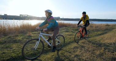 casal de homens e mulheres andam de bicicleta perto do rio durante o pôr do sol foto