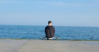 jovem macho com skate relaxante perto do mar foto