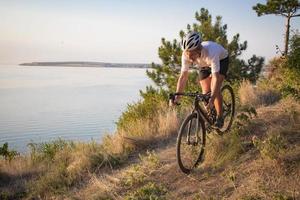 ciclista em passeio de bicicleta de ciclocross profissional em declive, pinheiro e fundo do lago foto