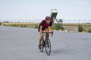 ciclista em treinamento de capacete e roupas esportivas sozinho na estrada rural vazia, campos e árvores foto