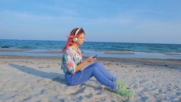 jovem com cabelo colorido anda na praia de verão e ouve música com fones de ouvido foto