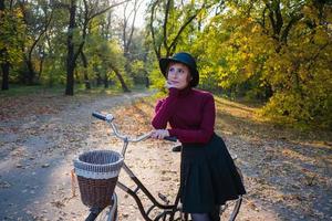 jovem no parque de outono leu livro, linda mulher ruiva com bicicleta na grama verde foto