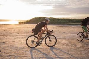 dois jovens do sexo masculino em uma bicicleta de turismo com mochilas e capacetes no deserto em uma viagem de bicicleta foto