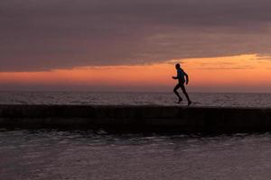 jovem em roupas de outono treinando na praia, fundo do nascer do sol, corredor masculino de manhã