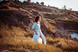 jovem caminhando na praia de manhã em lindo vestido branco. apto feminino se divertindo durante o nascer do sol. foto