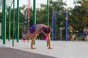 bela mulher apta no treinamento esportivo rosa e roxo na academia ao ar livre de manhã, exercícios com tiras de suspensão no parque foto