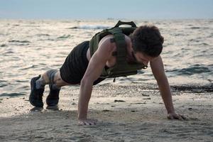 jovem atleta barbudo treinando ao ar livre com colete ponderado, exercício com portador de placa militar foto