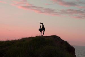 cabe a mulher fazendo exercícios de alongamento de ioga ao ar livre na paisagem de belas montanhas. fêmea na rocha com asans de treinamento de fundo mar e nascer ou pôr do sol. silhueta de mulher em poses de ioga foto