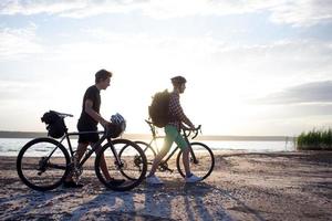 dois jovens do sexo masculino em uma bicicleta de turismo com mochilas e capacetes no deserto em uma viagem de bicicleta foto