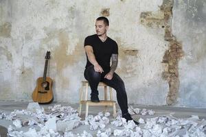 jovem macho com guitarra no quarto vazio, músico e compositor sozinho no estúdio foto