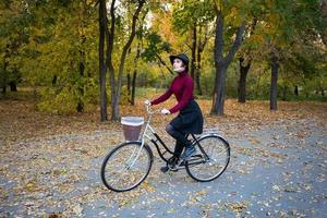 jovem no parque de outono leu livro, linda mulher ruiva com bicicleta na grama verde foto