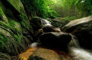 bela cachoeira na selva. cachoeira na floresta tropical com árvore verde e luz solar. cachoeira está fluindo na selva. fundo da natureza. rocha ou pedra na cachoeira. viagens de temporada verde na tailândia foto